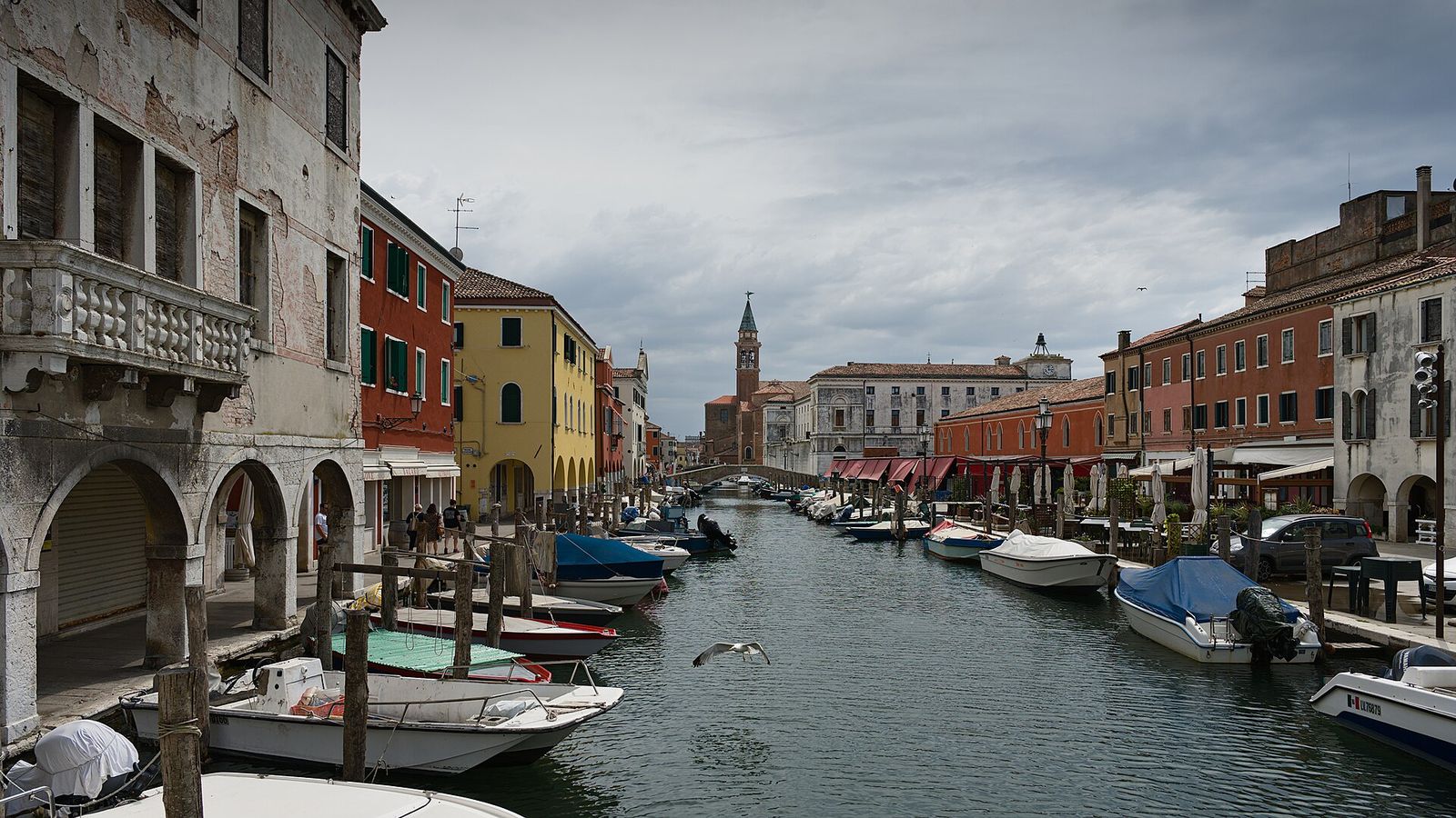 Canal Vena in Chioggia, lined with moored boats and arcaded houses, with a church tower at the far end