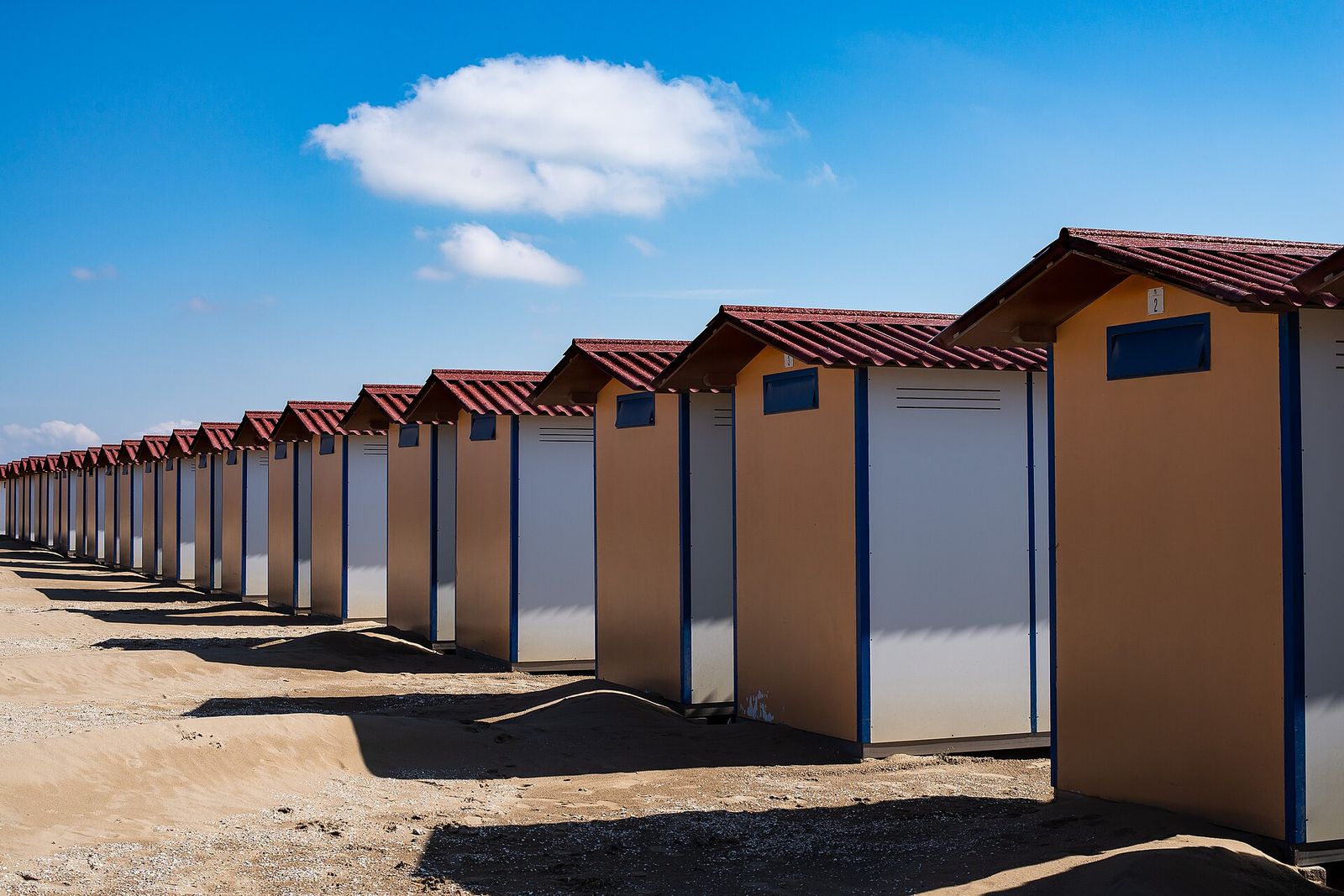 A long row of beach cabins with red roofs on the sand at the Lido